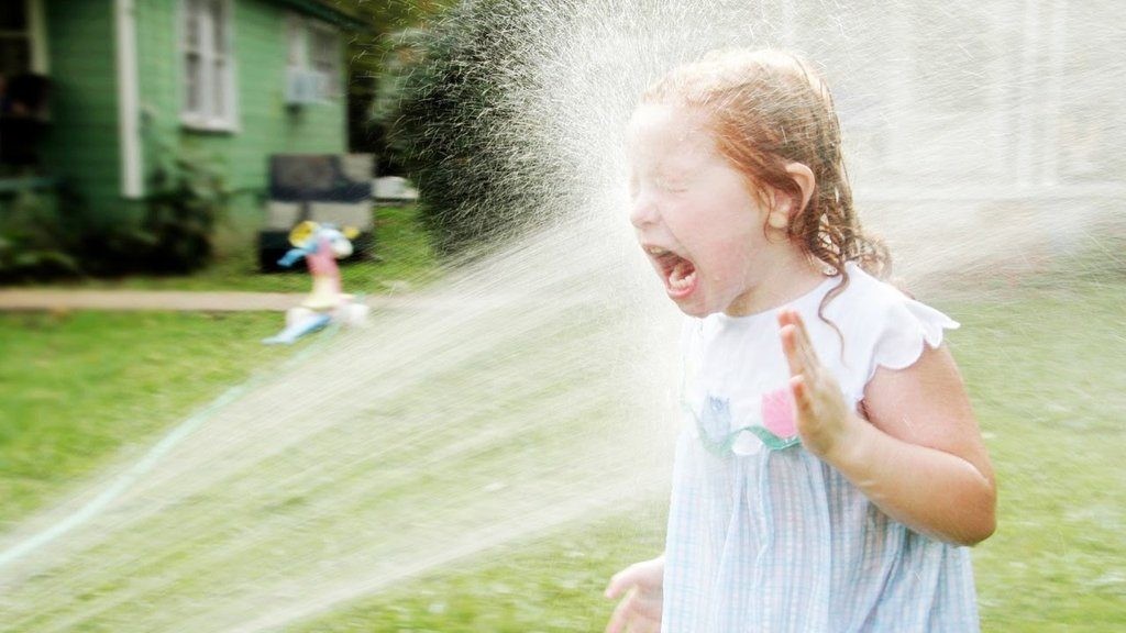 small girl with strong stream of water hitting her in the face